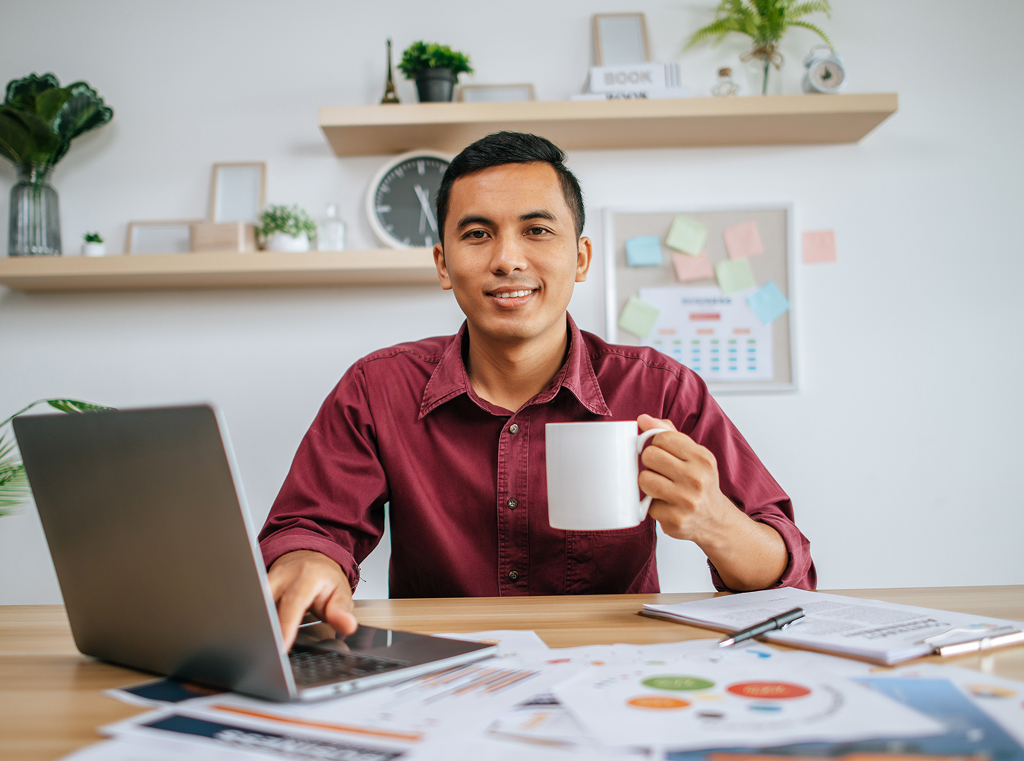 Man working on a laptop while holding a coffee cup at his desk